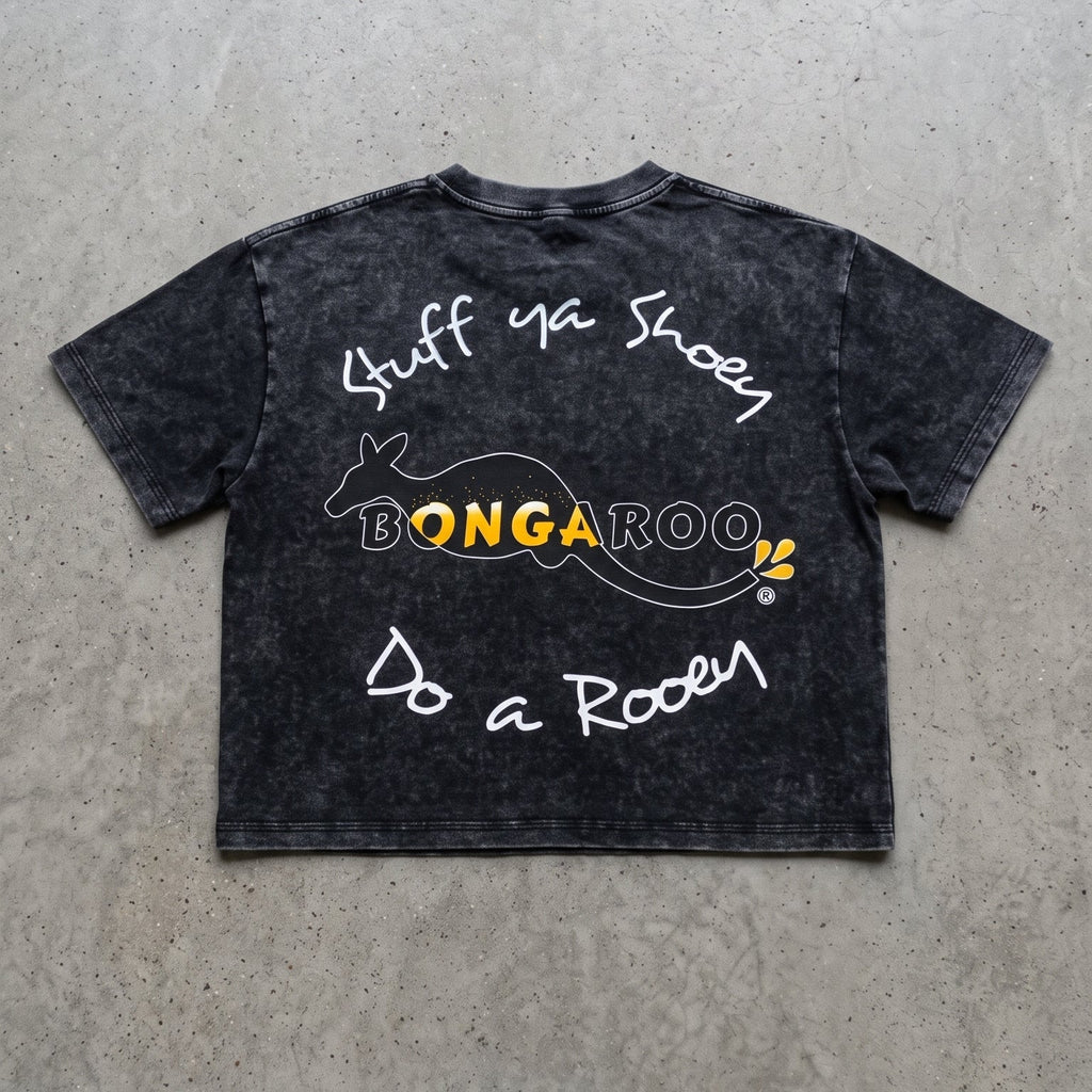 A black acid-wash graphic t-shirt laid flat on a textured gray concrete background. The shirt features white handwritten-style text reading 'Stuff Ya Shoes' and 'Do a Roar' with a central yellow and white 'BONGAROO' logo.