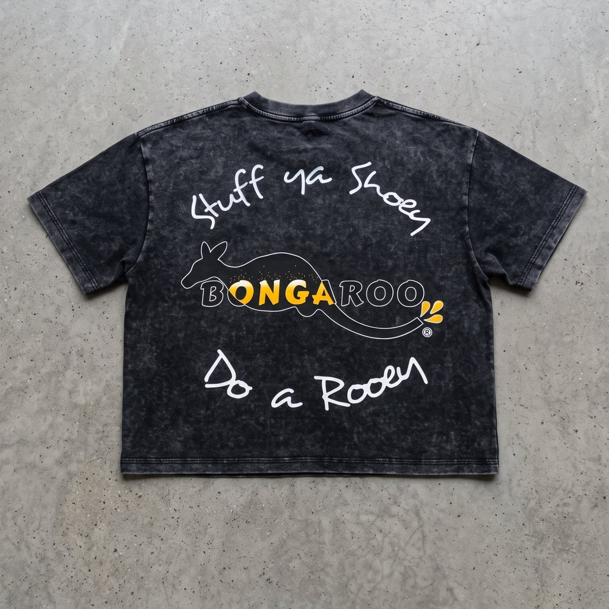 A black acid-wash graphic t-shirt laid flat on a textured gray concrete background. The shirt features white handwritten-style text reading 'Stuff Ya Shoes' and 'Do a Roar' with a central yellow and white 'BONGAROO' logo.